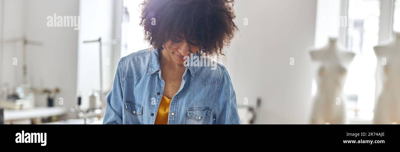 Professional African-American dressmaker draws pattern on fabric working at cutting table Stock Photo