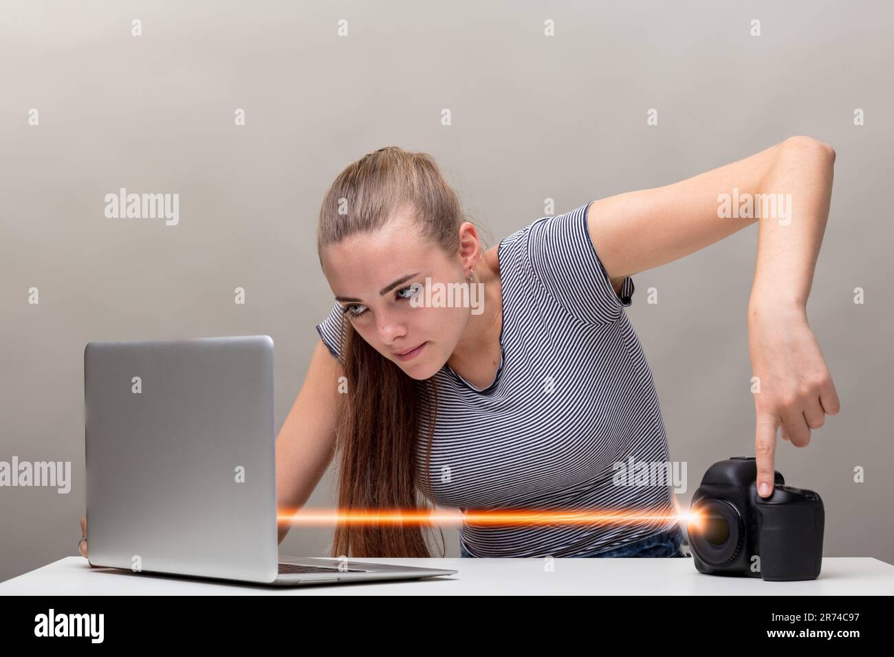 A focused woman, hair tied back and in a striped shirt, wirelessly transfers photo and video files from her digital camera to her laptop. She hits the Stock Photo