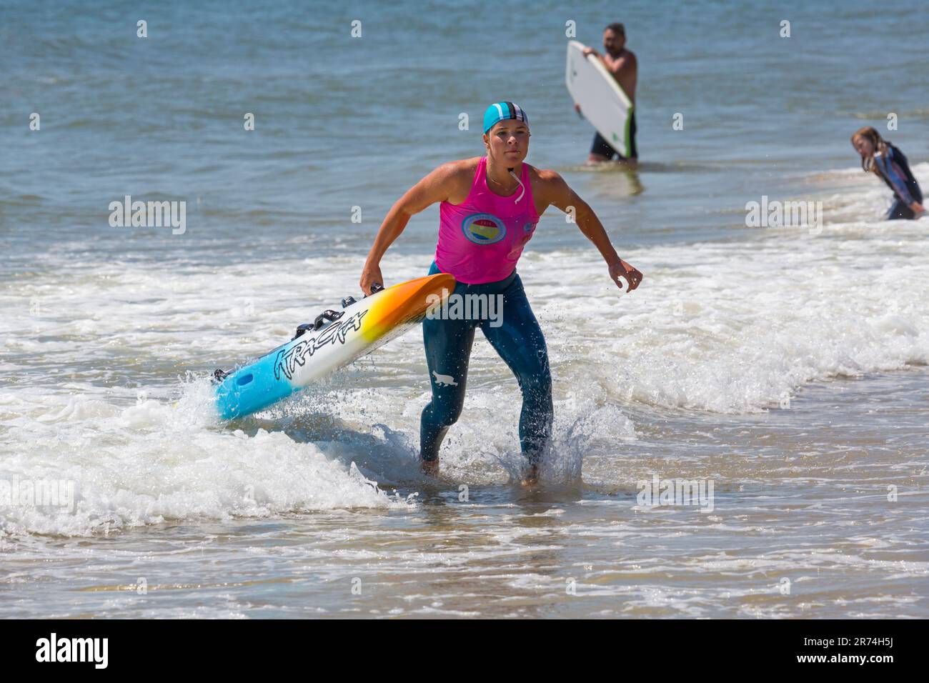 Young woman carrying paddle board paddleboard, the Surf Life Saving GB GBR Beach Trial Weekend at Branksome Chine, Poole, Dorset, England UK in June Stock Photo