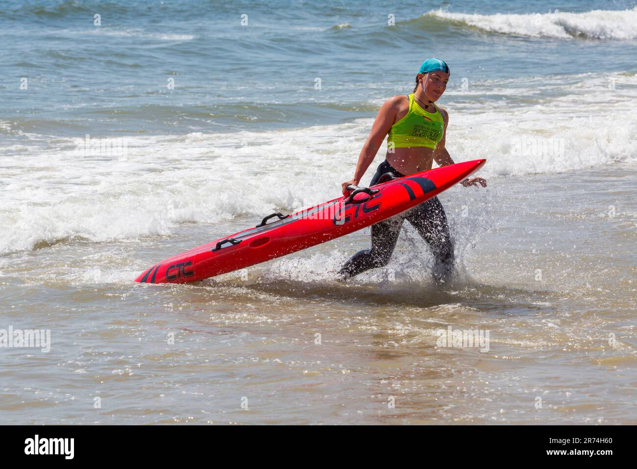 Young woman carrying paddle board paddleboard, the Surf Life Saving GB GBR Beach Trial Weekend at Branksome Chine, Poole, Dorset, England UK in June Stock Photo