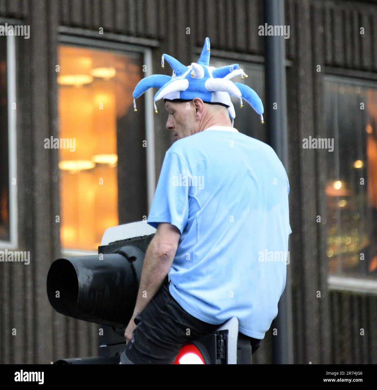 Manchester, UK. 12th June, 2023. A Man City fan sits on a traffic light to see the open top bus victory parade celebration in central Manchester, UK, to mark the achievement of their club winning the treble: the Premier League, the FA Cup, and the Champions League. On Saturday Man City beat Inter Milan in Istanbul to secure the Champions League win. The parade of open top buses went through Manchester city centre watched by large, enthusiastic crowds, despite a thunderstorm and heavy rain. Credit: Terry Waller/Alamy Live News Stock Photo