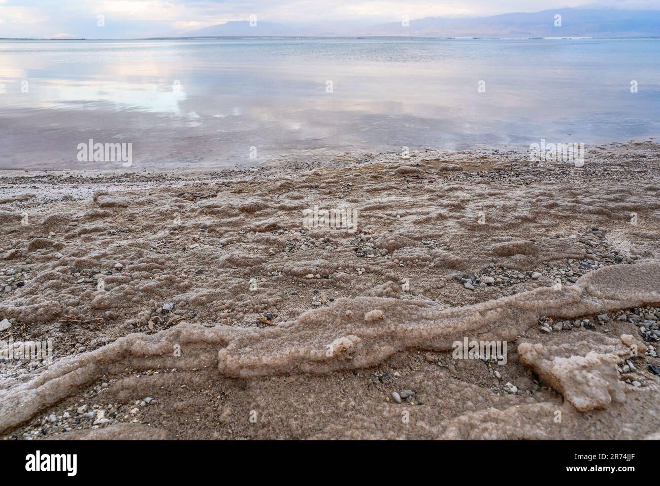 Sand and stones covered with crystalline salt on shore of Dead Sea, clear water background - typical morning scenery at Ein Bokek beach, Israel Stock Photo
