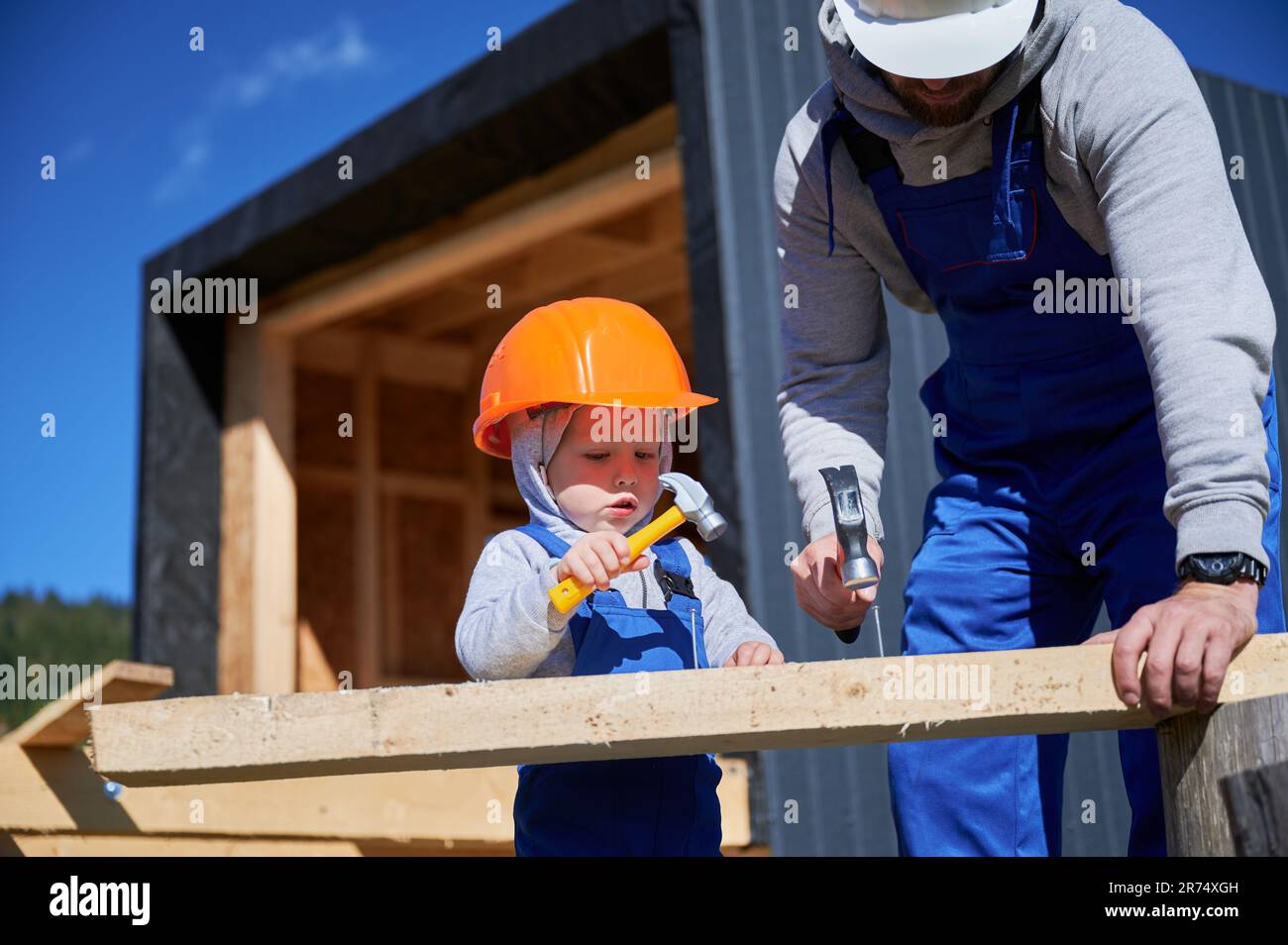 Father with toddler son building wooden frame house. Boy helping his