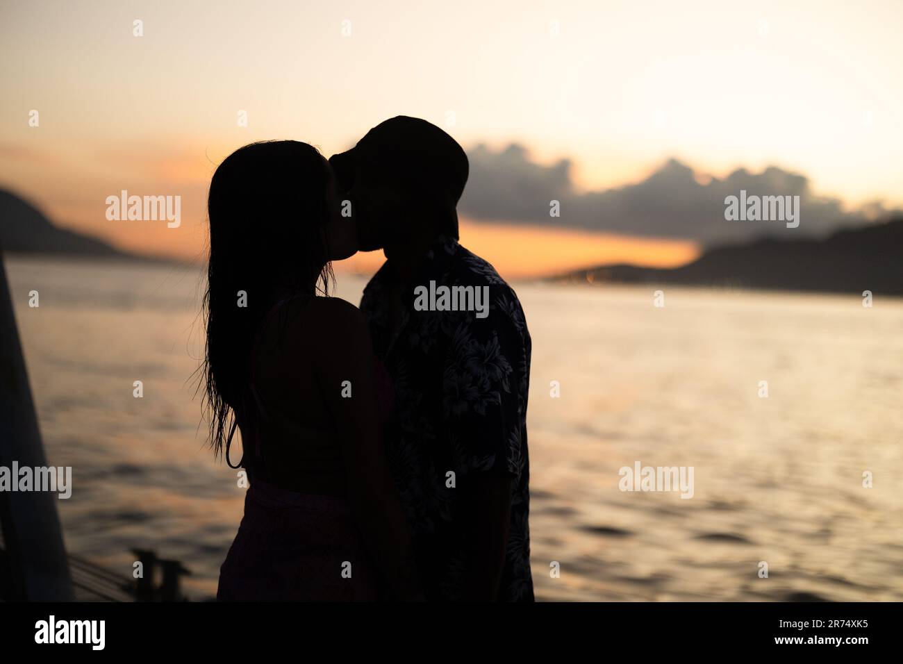 A silhouette of a loving couple kissing against a sunset sea background ...