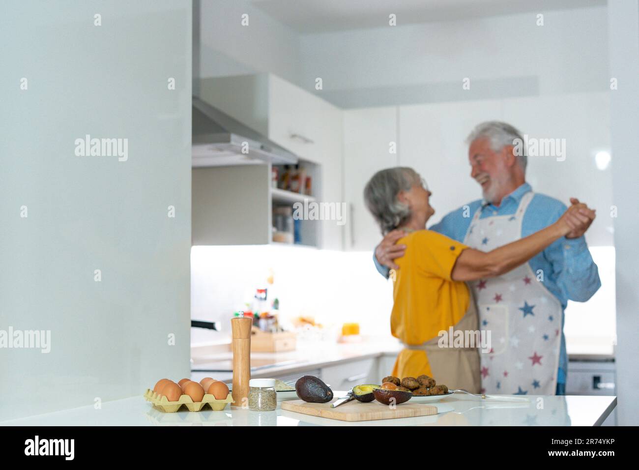 Full length energetic middle aged family couple dancing to disco music in kitchen. Happy old mature man and woman having fun, entertaining together indoors, involved in funny domestic activity. Stock Photo