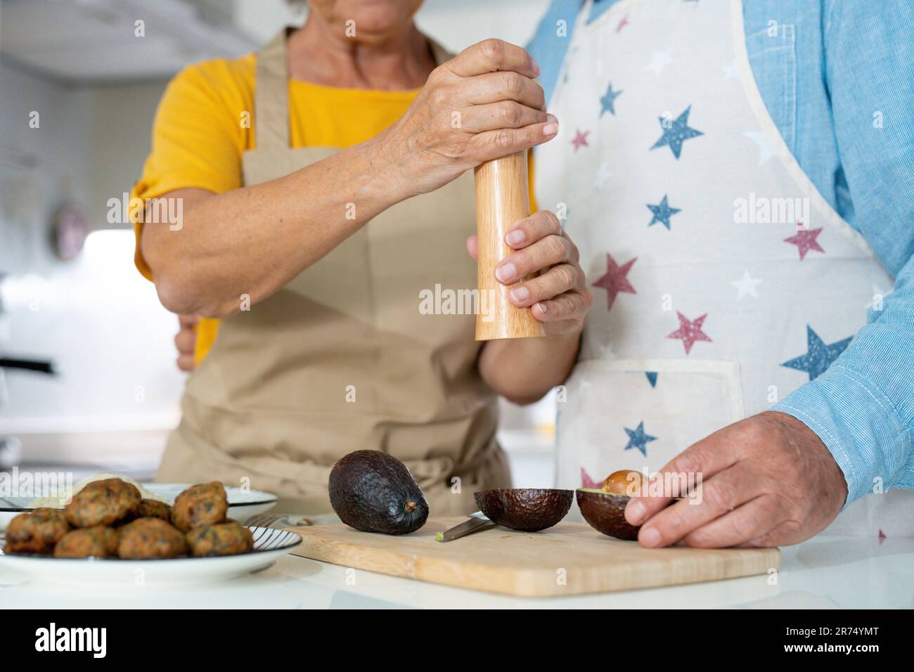 Happy joyful older husband and wife sharing cooking chores, making organic fresh salad together, cutting vegetables, talking, laughing. Old couple having fun in kitchen, preparing dinner Stock Photo