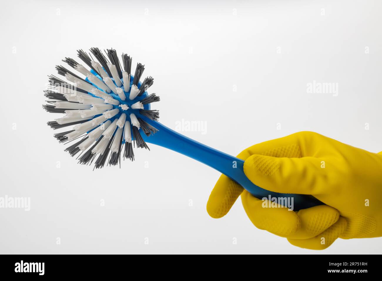 Hand with yellow protective glove holds blue dishwashing brush, white background, Stock Photo