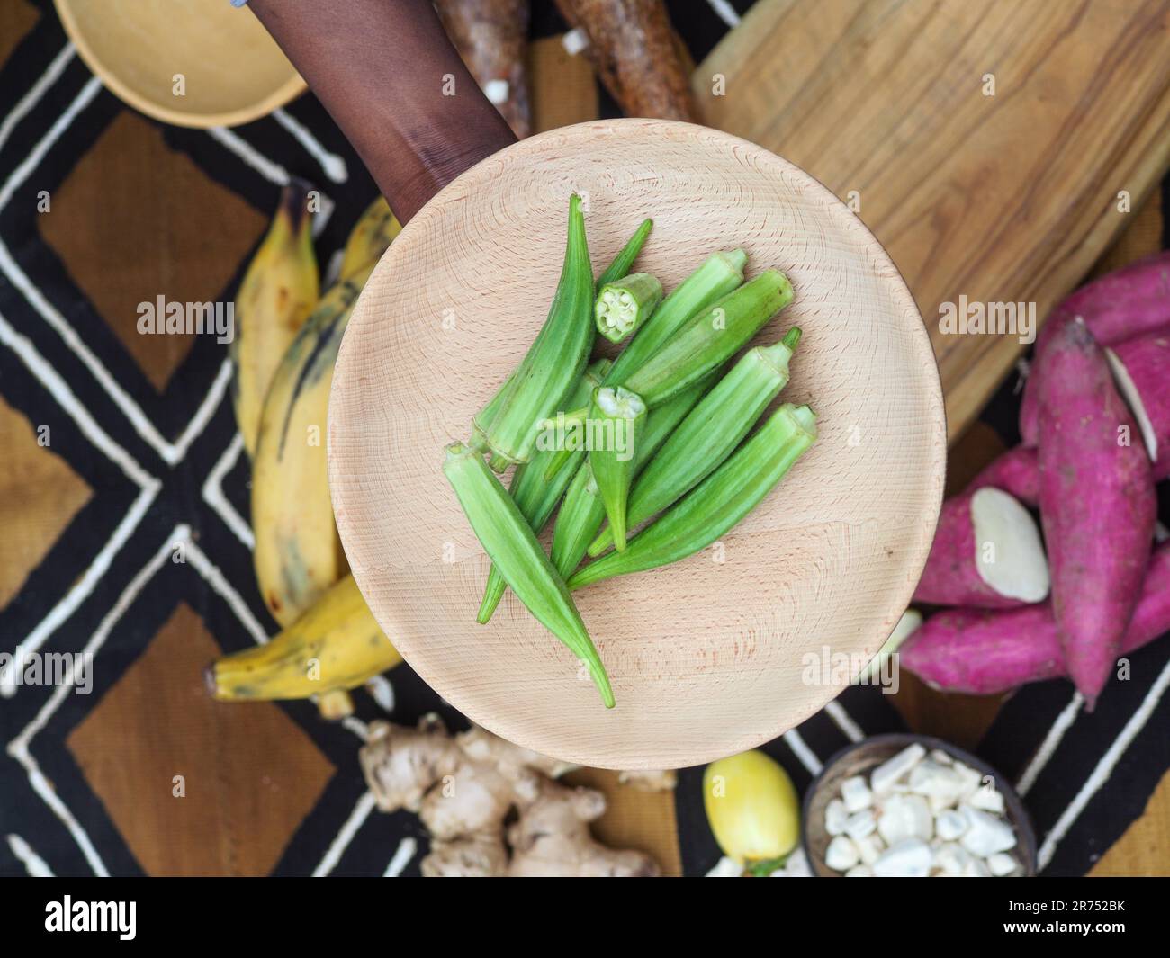 african woman chopping okra fruit veggies to cook traditional recipe with other local veggies and fruits. Stock Photo