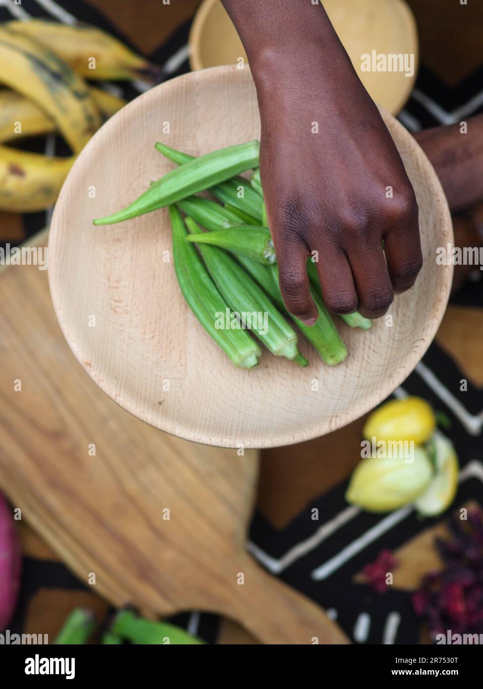 african woman chopping okra fruit veggies to cook traditional recipe with other local veggies and fruits. Stock Photo