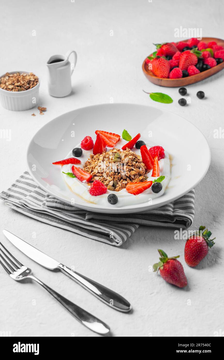 A vertical closeup of yogurt with granola and fruits on a white