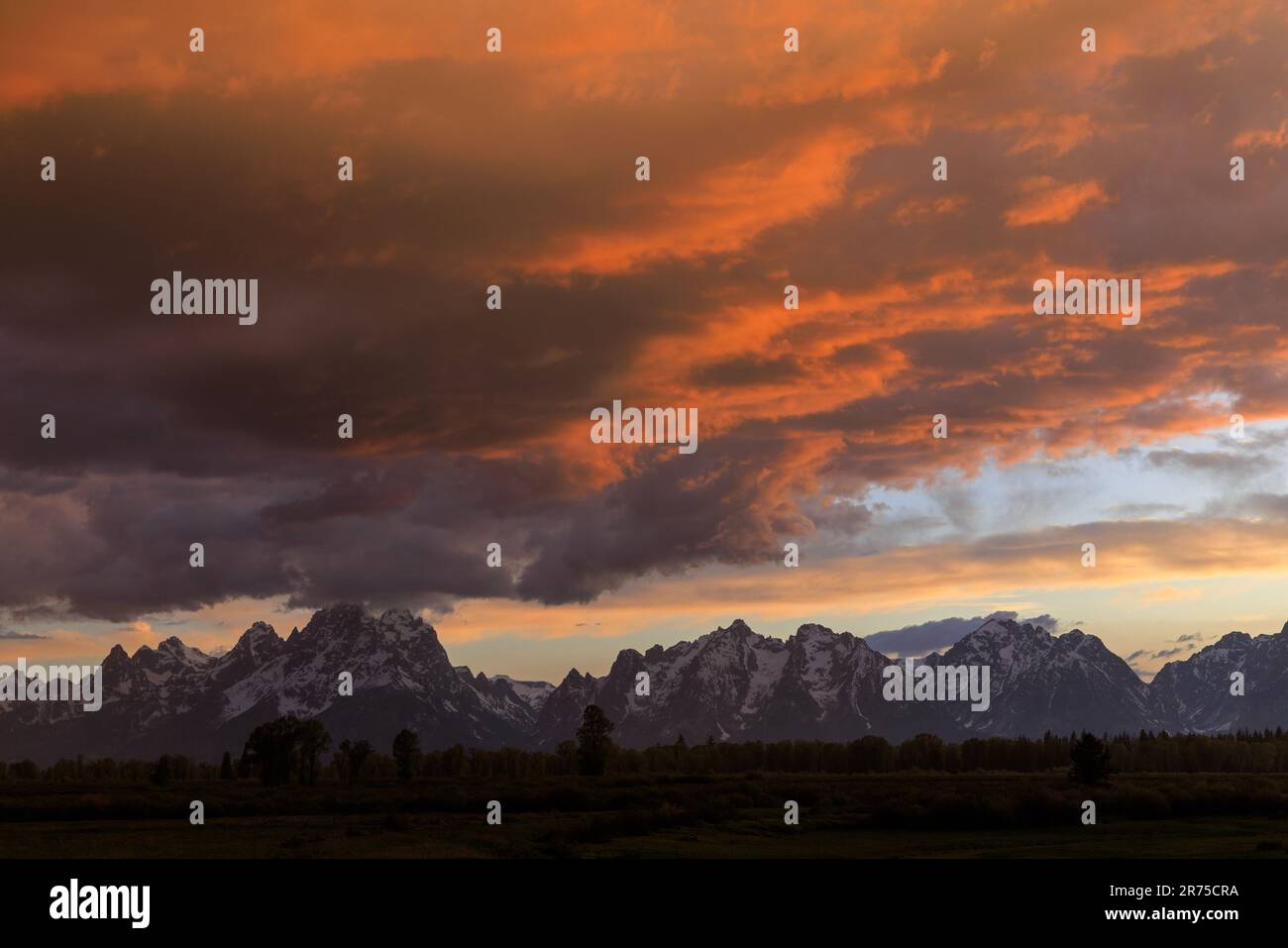 The setting sun lights up the clouds over Grand Teton National Park, Teton County, Wyoming, USA. The Teton Range is in the distance. Stock Photo