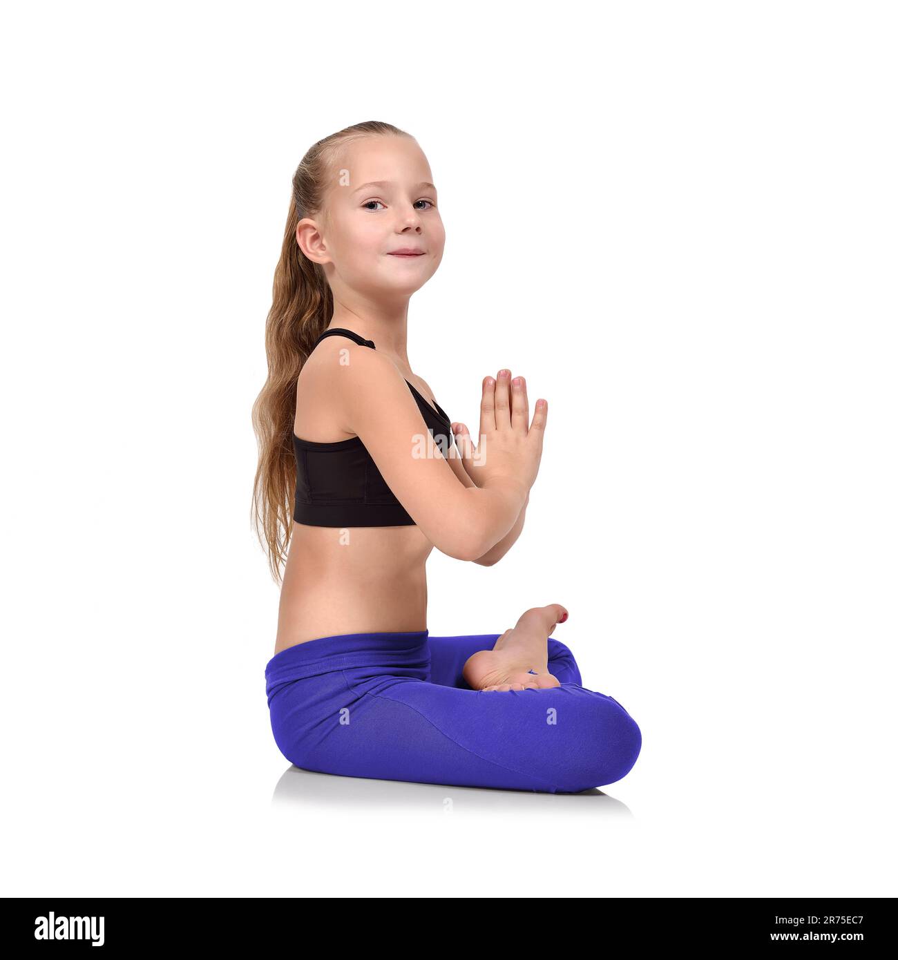 Cute little girl sitting on fitness mat in a lotus position while