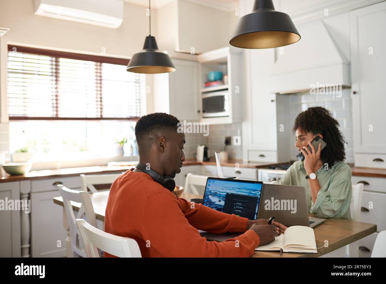 Young multiracial couple working remotely at a kitchen table Stock Photo