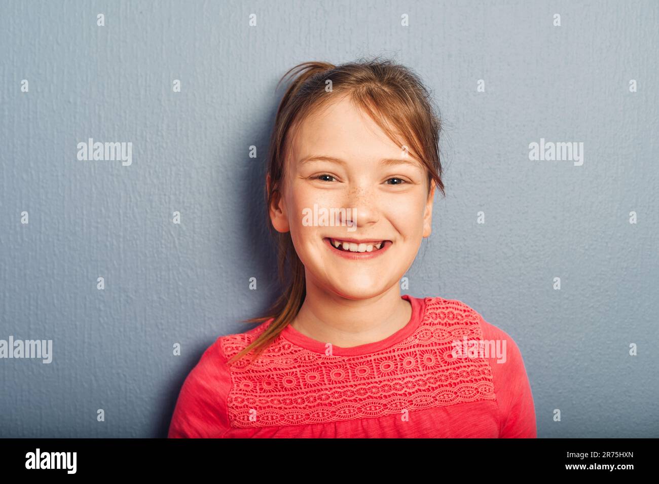 Portrait of young preteen 9-10 year old girl wearing pink top, standing against blue purple background Stock Photo
