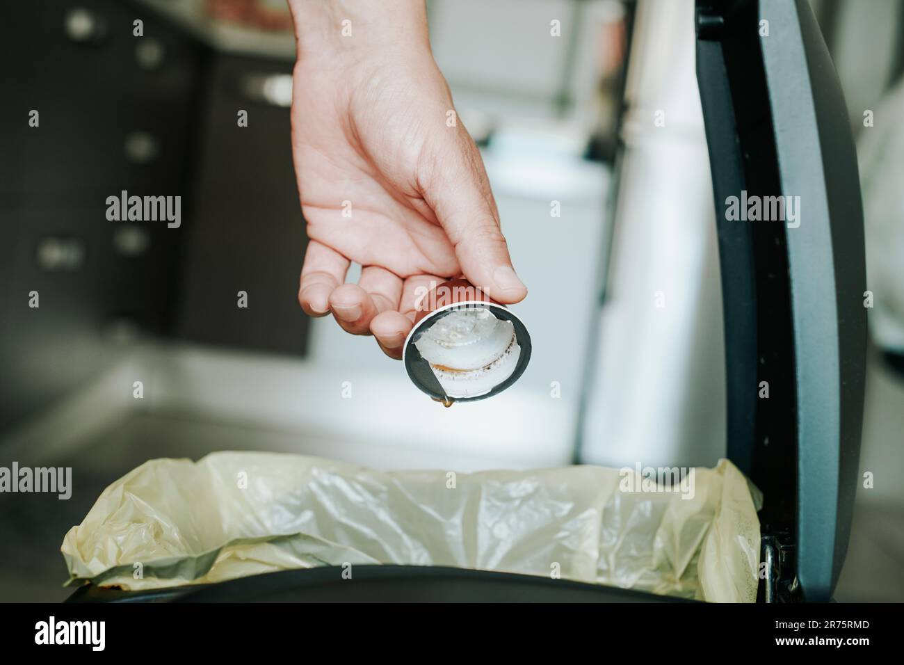 a caucasian man, in the kitchen, throws an emptied coffee capsule to the recyclable waste dustbin Stock Photo