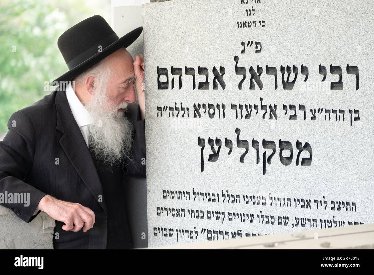 An older Jewish man engages in fervent prayer near the headstone of a former leader of the Skolya Hasidic dynasty. In a cemetery in Monsey, New York. Stock Photo