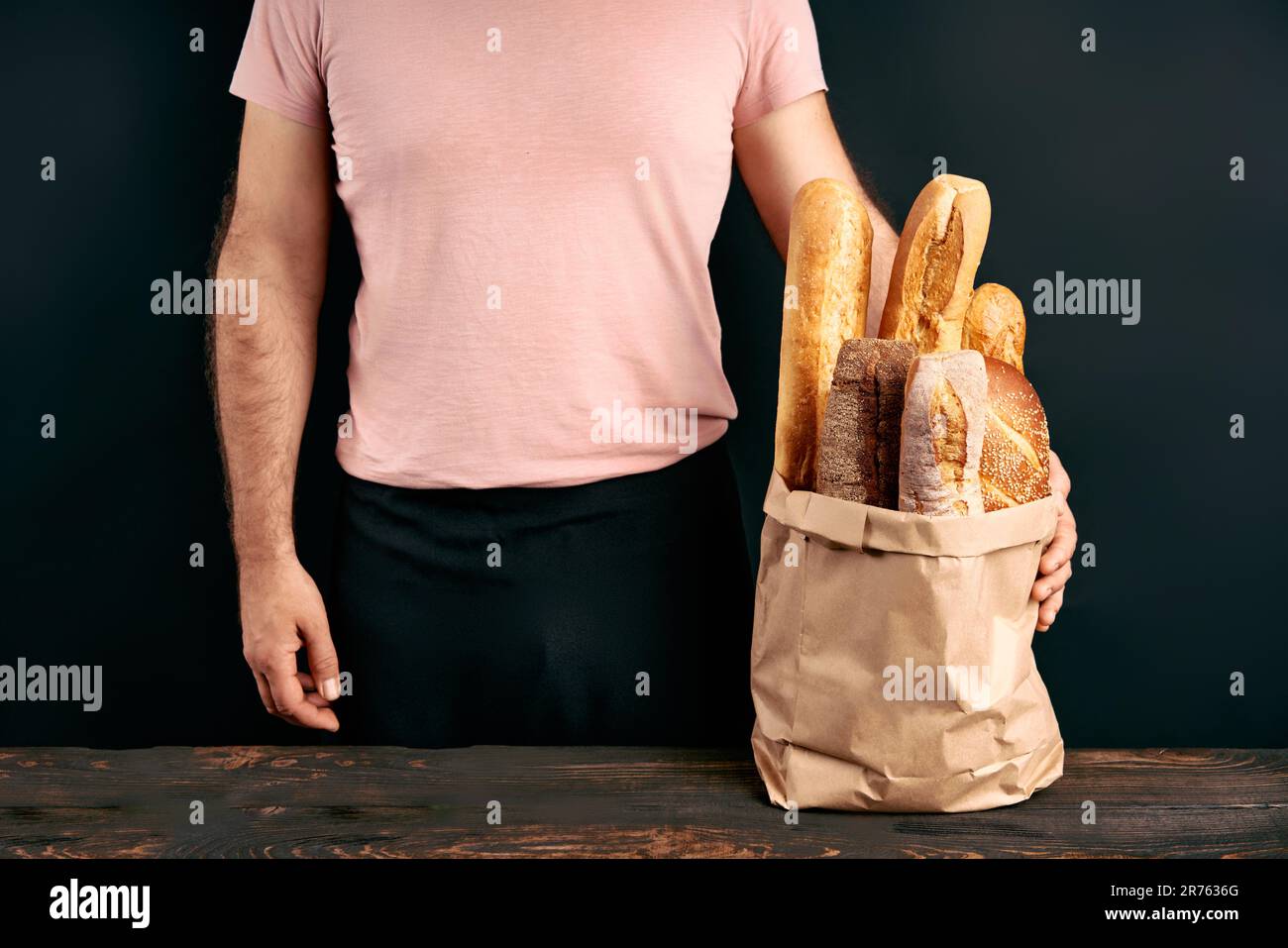 Man holds fresh loaves of bread baguettes in paper bag over light background. Bakery, food concept Stock Photo