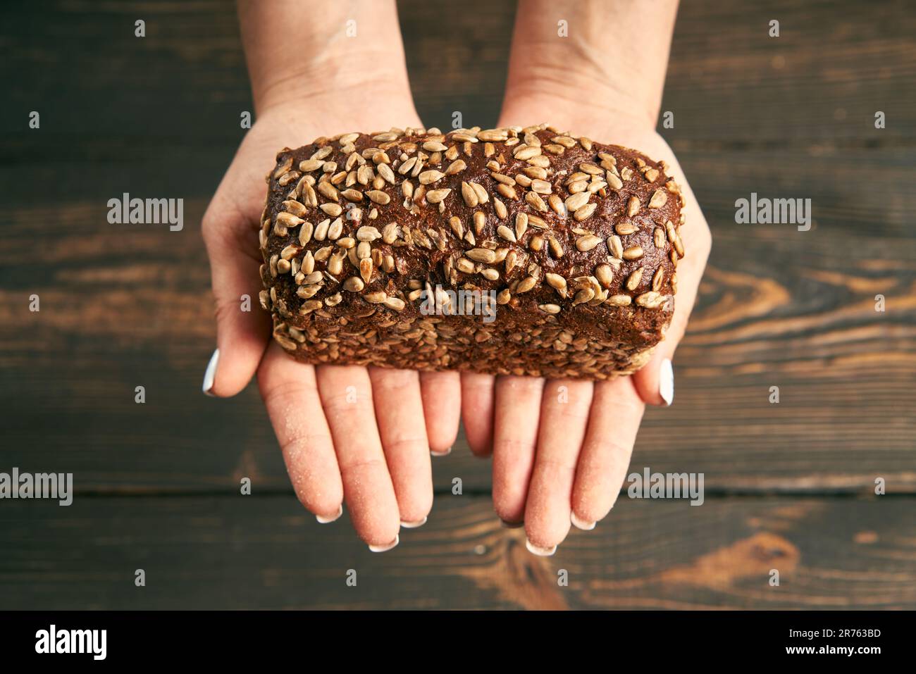 Loaf of fresh made rye multigrain bread in woman hands on wooden table background. Bakery, food concept Stock Photo