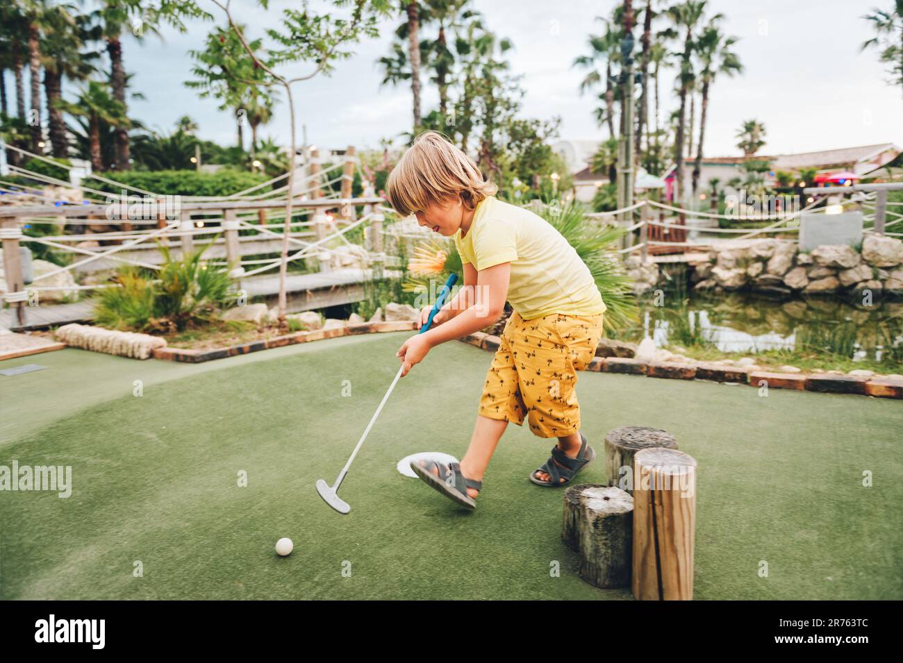 Funny kid boy playing mini golf, child enjoying summer vacation Stock Photo