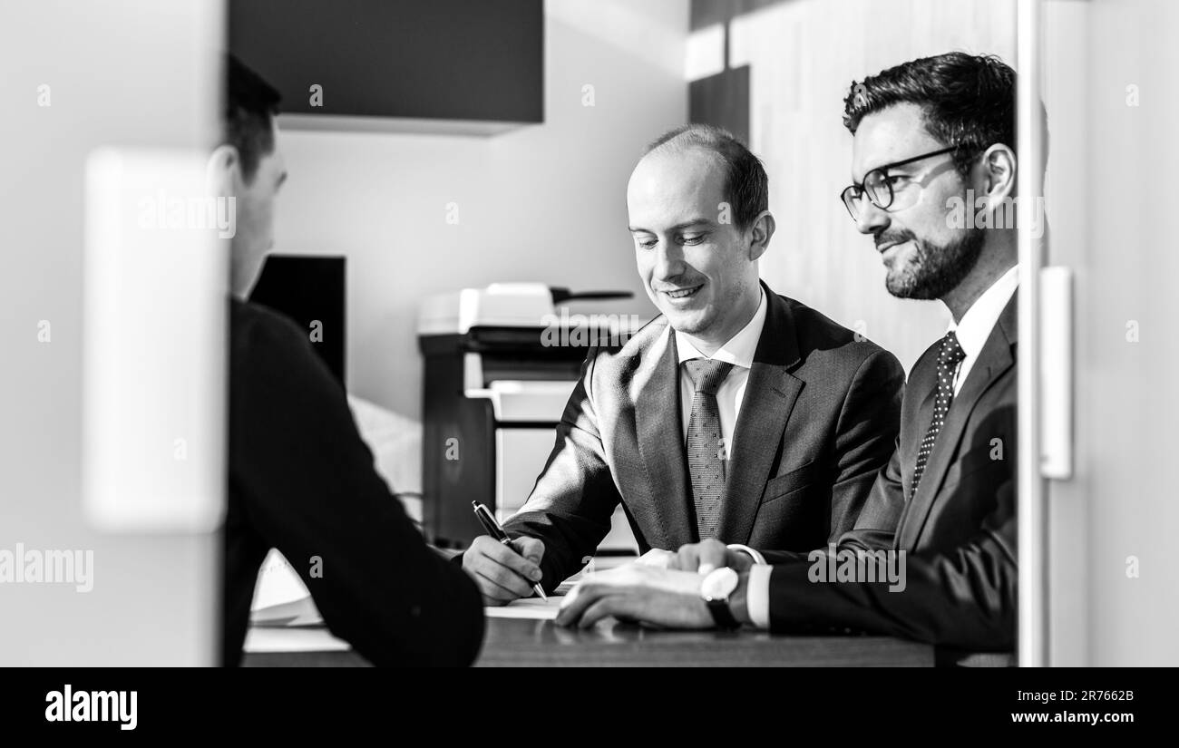 Team of confident successful business people reviewing and signing a contract to seal the deal at business meeting in modern corporate office. Business concept. Black and white image. Stock Photo