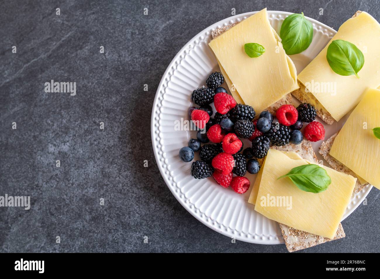 Healthy breakfast with low carb crispbread, old gouda cheese and fresh berries isolated on dark background. Top view Stock Photo