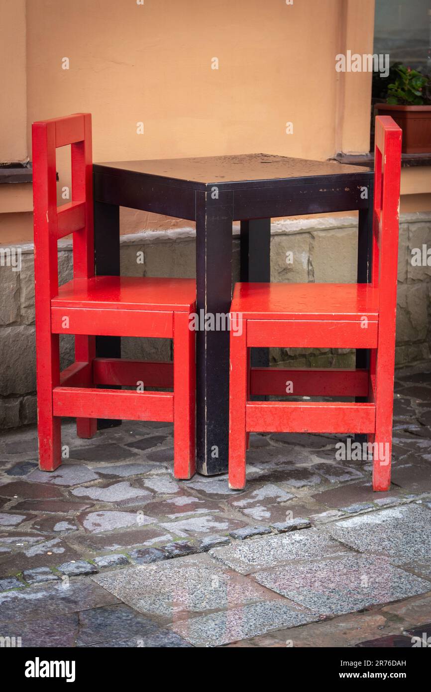 Outdoor cafe furniture. Empty wooden table and red chairs near restaurant window. Sidewalk cafe. Big city life. Vintage style of furniture Stock Photo