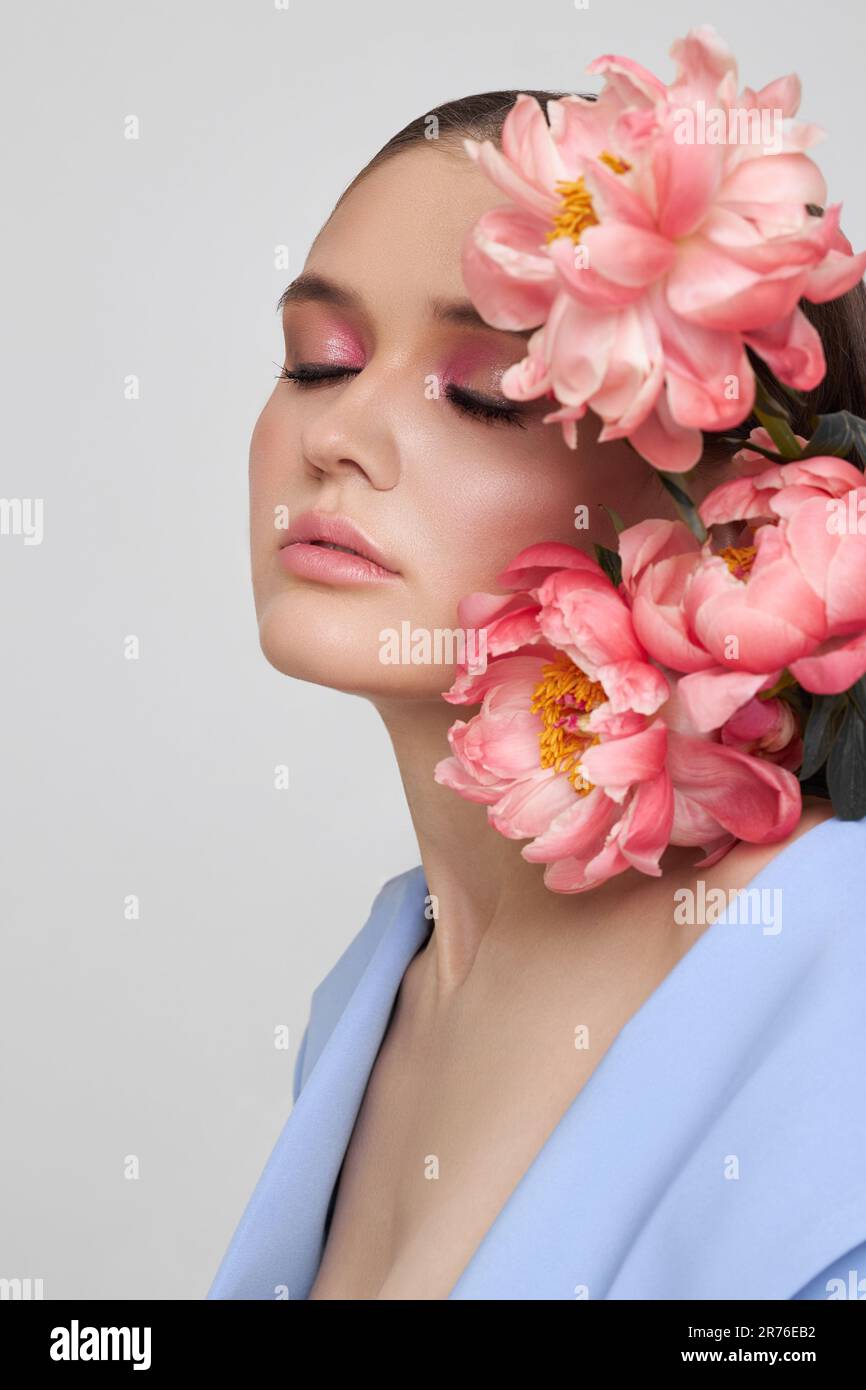 Fashion woman in blue suit with pink flowers, beauty face portrait. Art studio portrait of a young woman on a white background, pink makeup Stock Photo