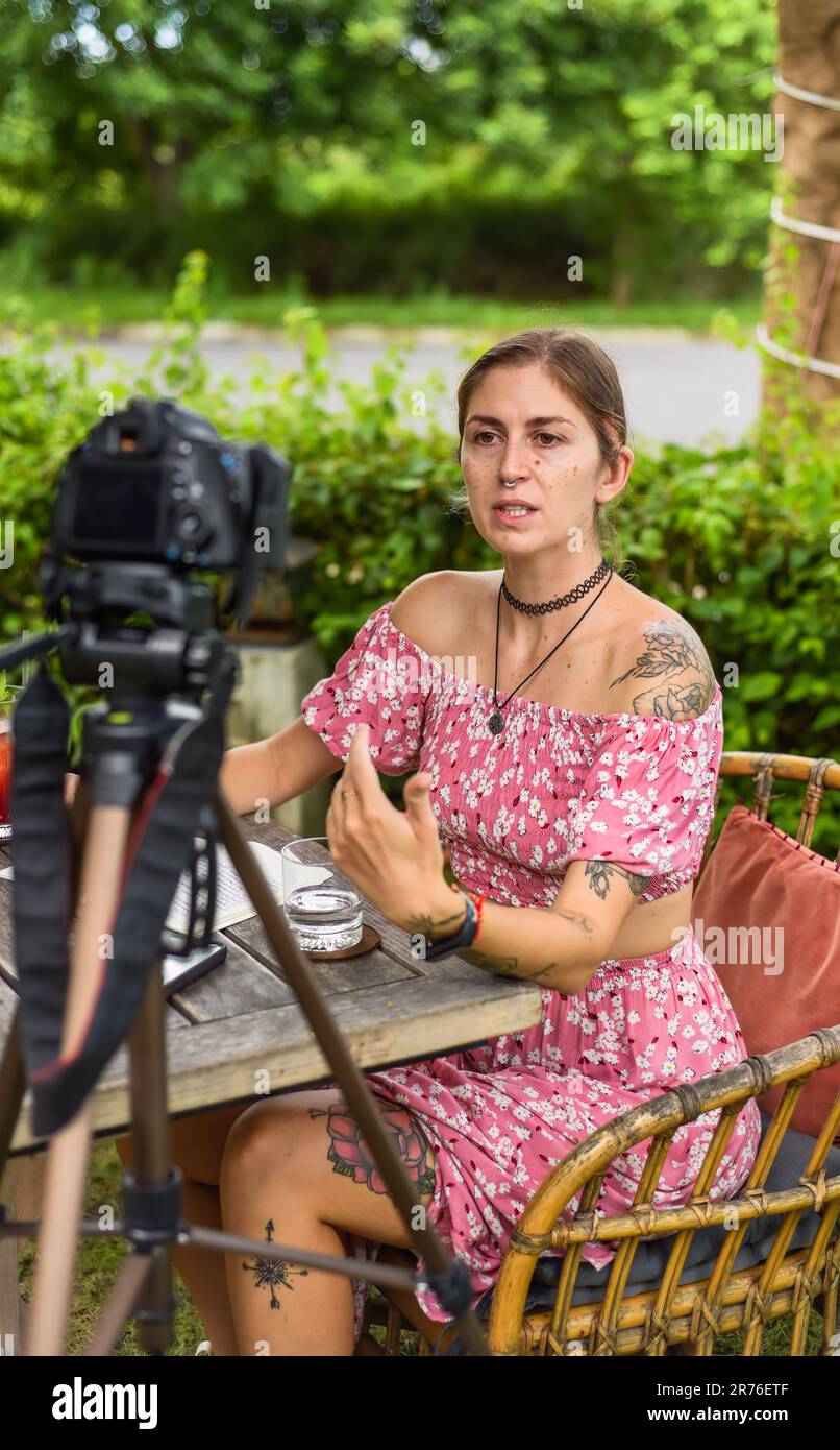 Cute videographer and vlogger taking a video with camera and tripod in summer garden Stock Photo