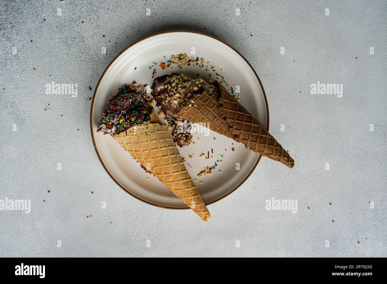 High angle waffle cones with coffee and chocolate ice cream with multicolored sugar and nuts on a ceramic plate Stock Photo