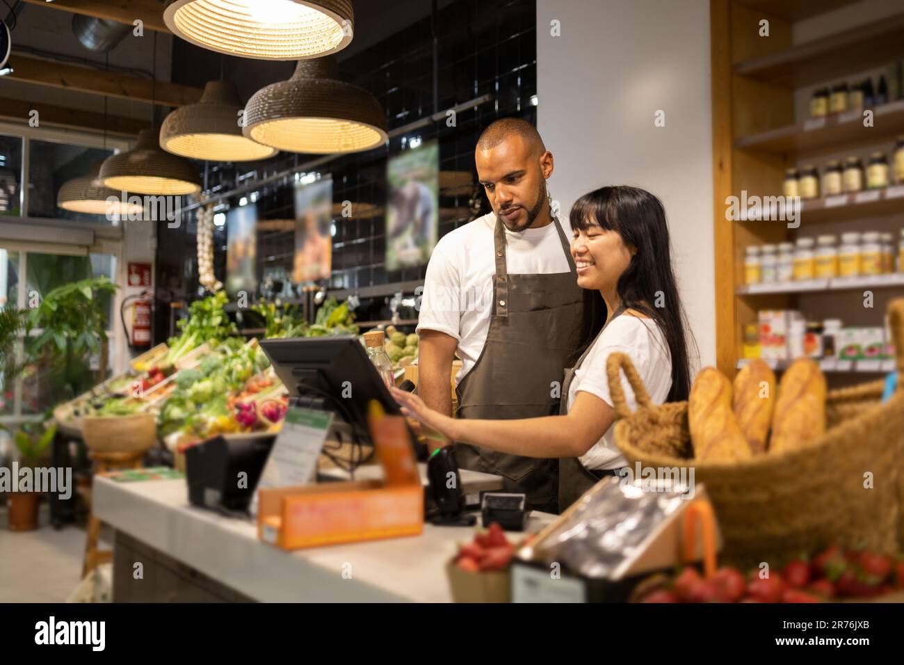 Happy young multiracial coworkers in aprons smiling and using monitor ...