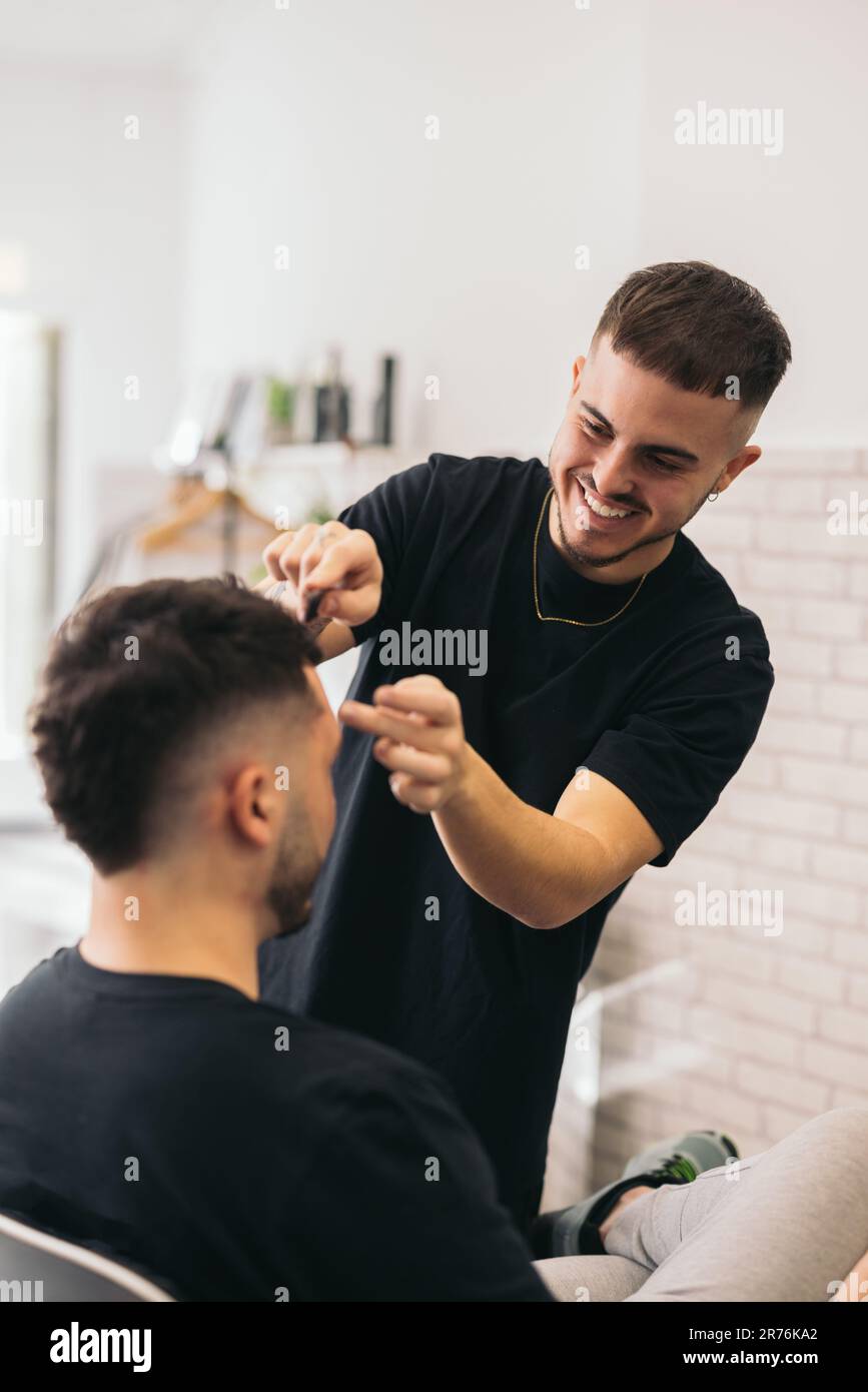 Front view of young barber combing unrecognizable man in barber shop against blurred background Stock Photo