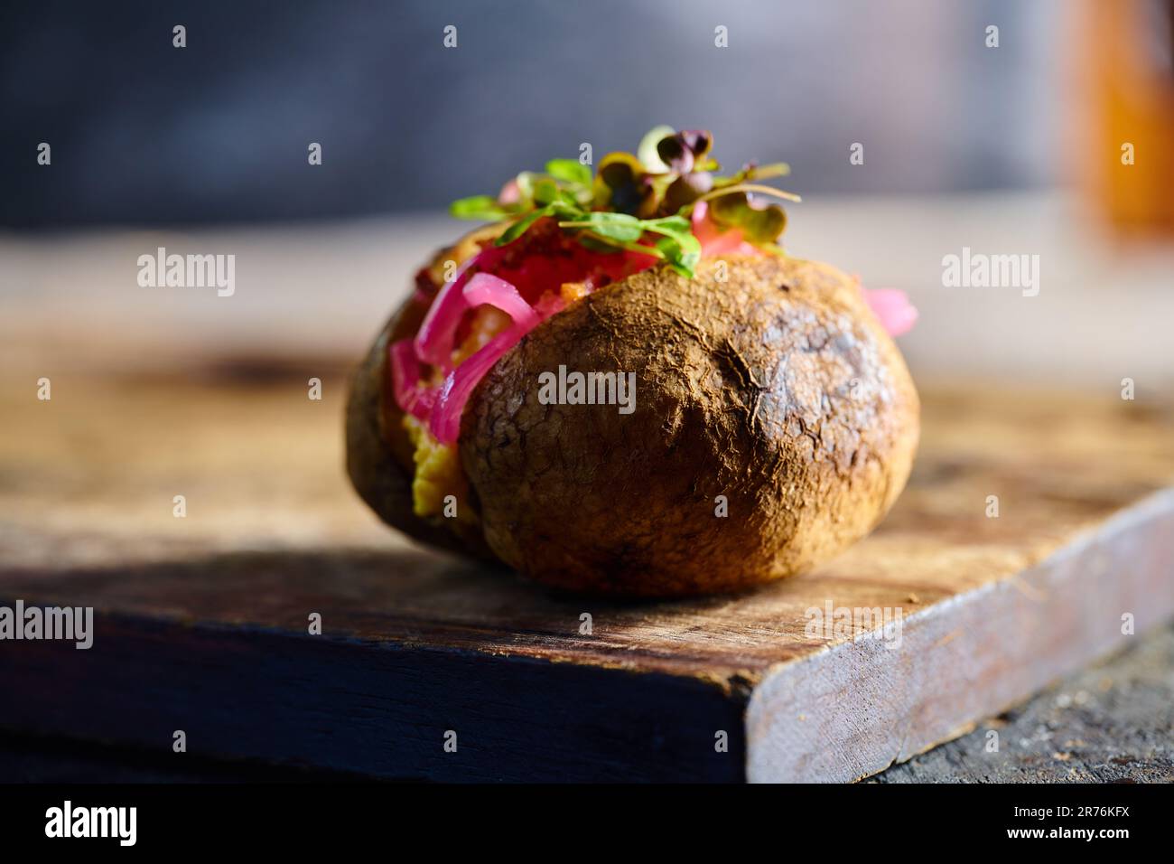 Appetizing traditional Ecuadorian kumpir potato with stuffing and herbs placed on wooden cutting board against blurred background Stock Photo