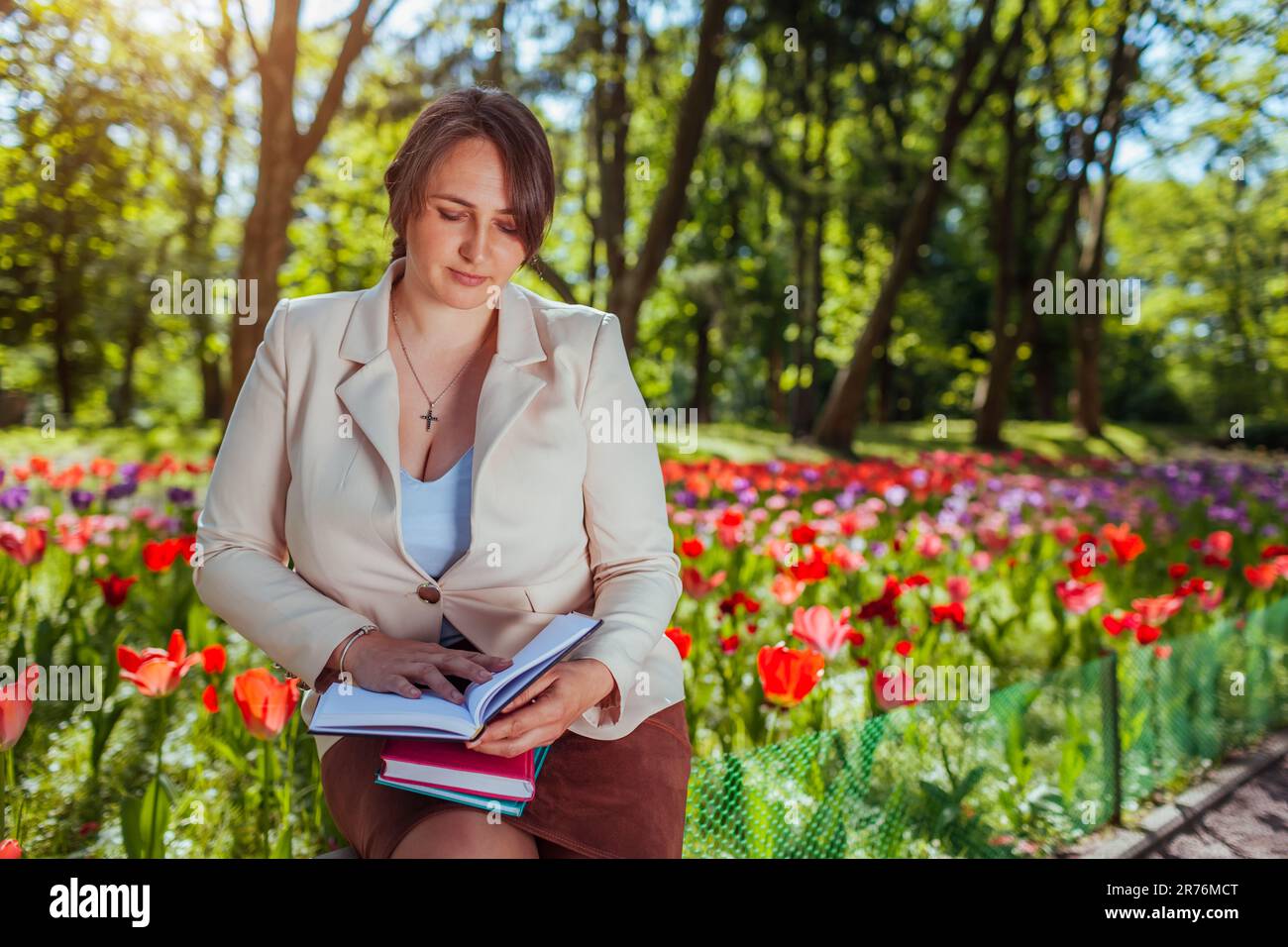 Young caucasian business woman ckecking notes in spring park. Teacher having break outdoors. Landscape designer working outdoors Stock Photo