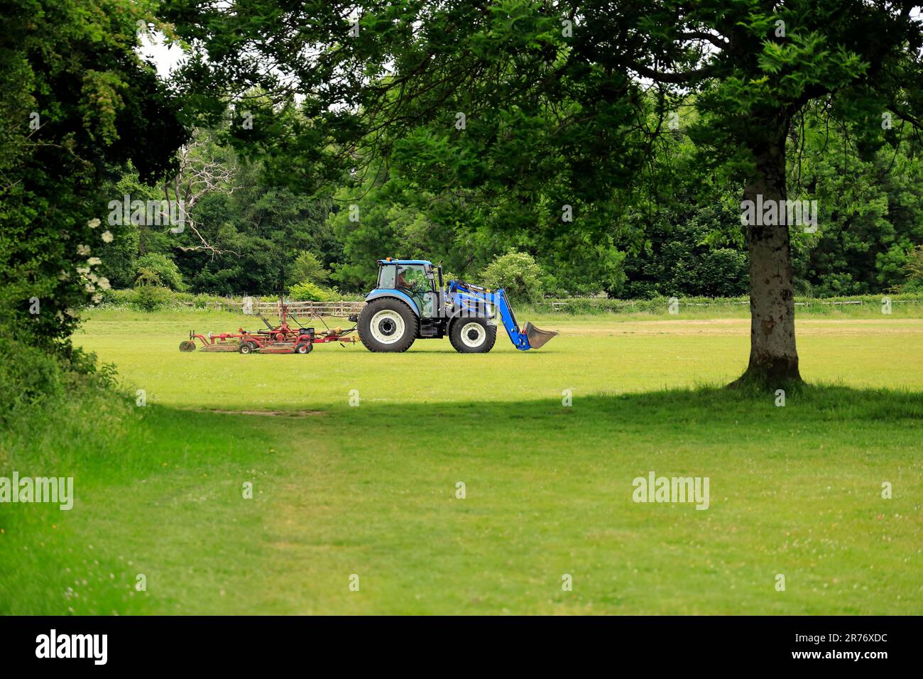 Blue Tractor Smoothing the Ground in a Farm with Trees and Grass
