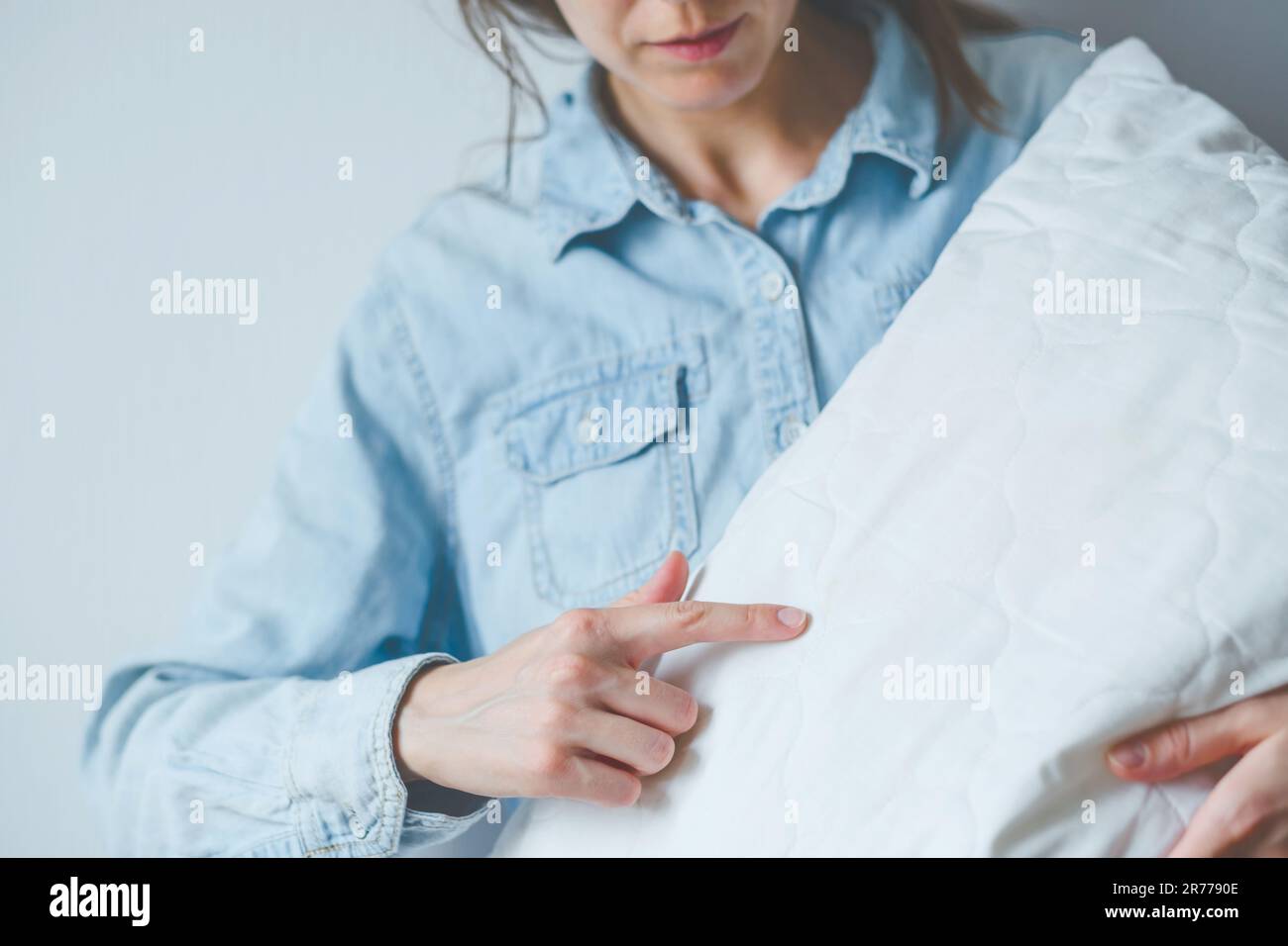 Faceless female pointing finger bed bugs on a white pillow. Health