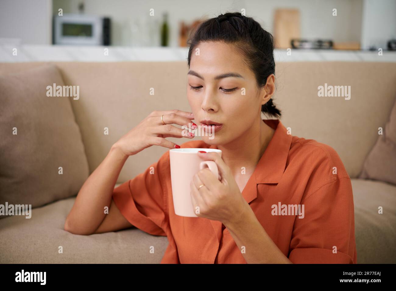 Young woman blowing on cup and drinking hot coffee while resting at home Stock Photo