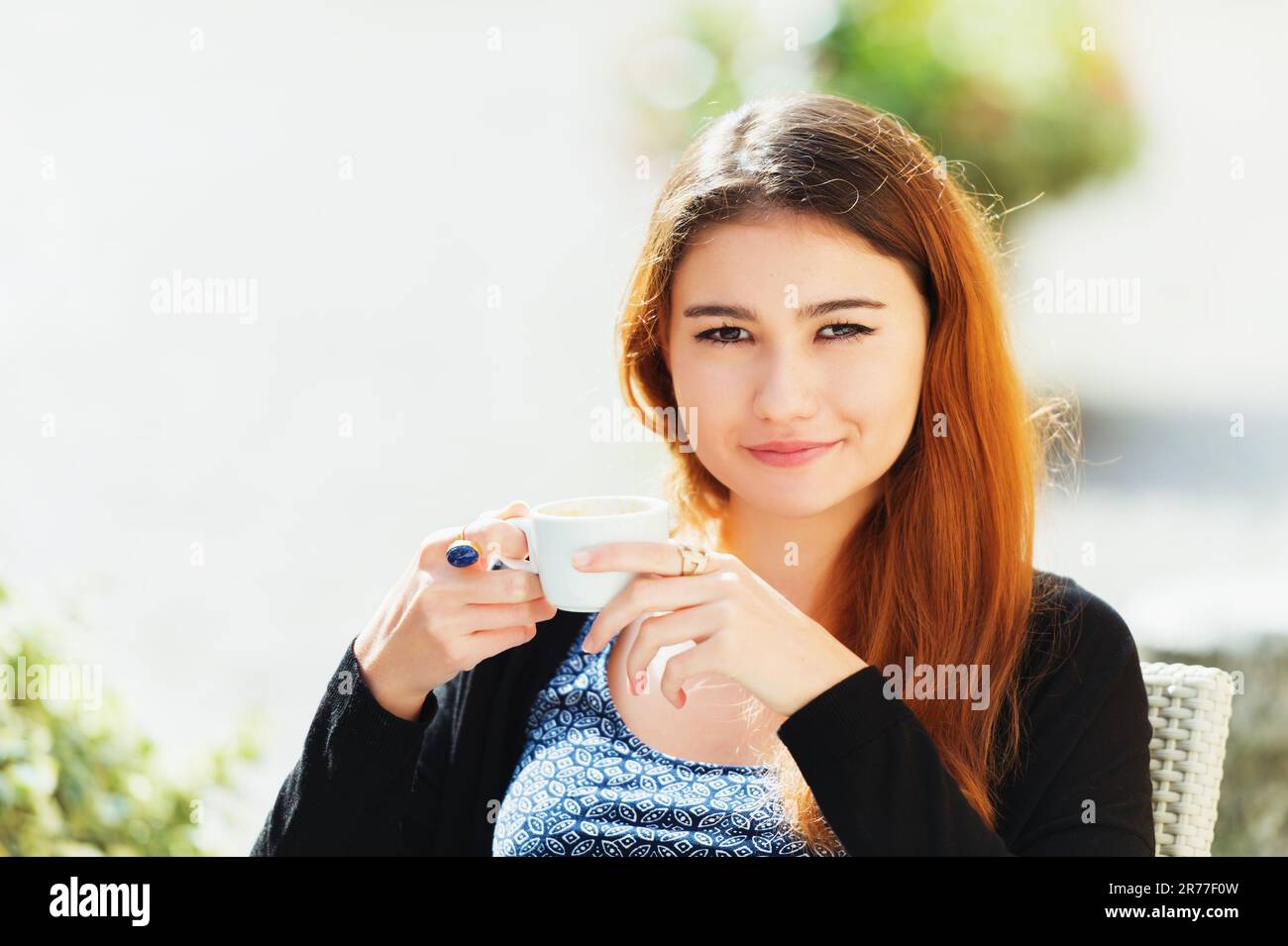Young woman drinking coffee at cafe on sunny day Stock Photo