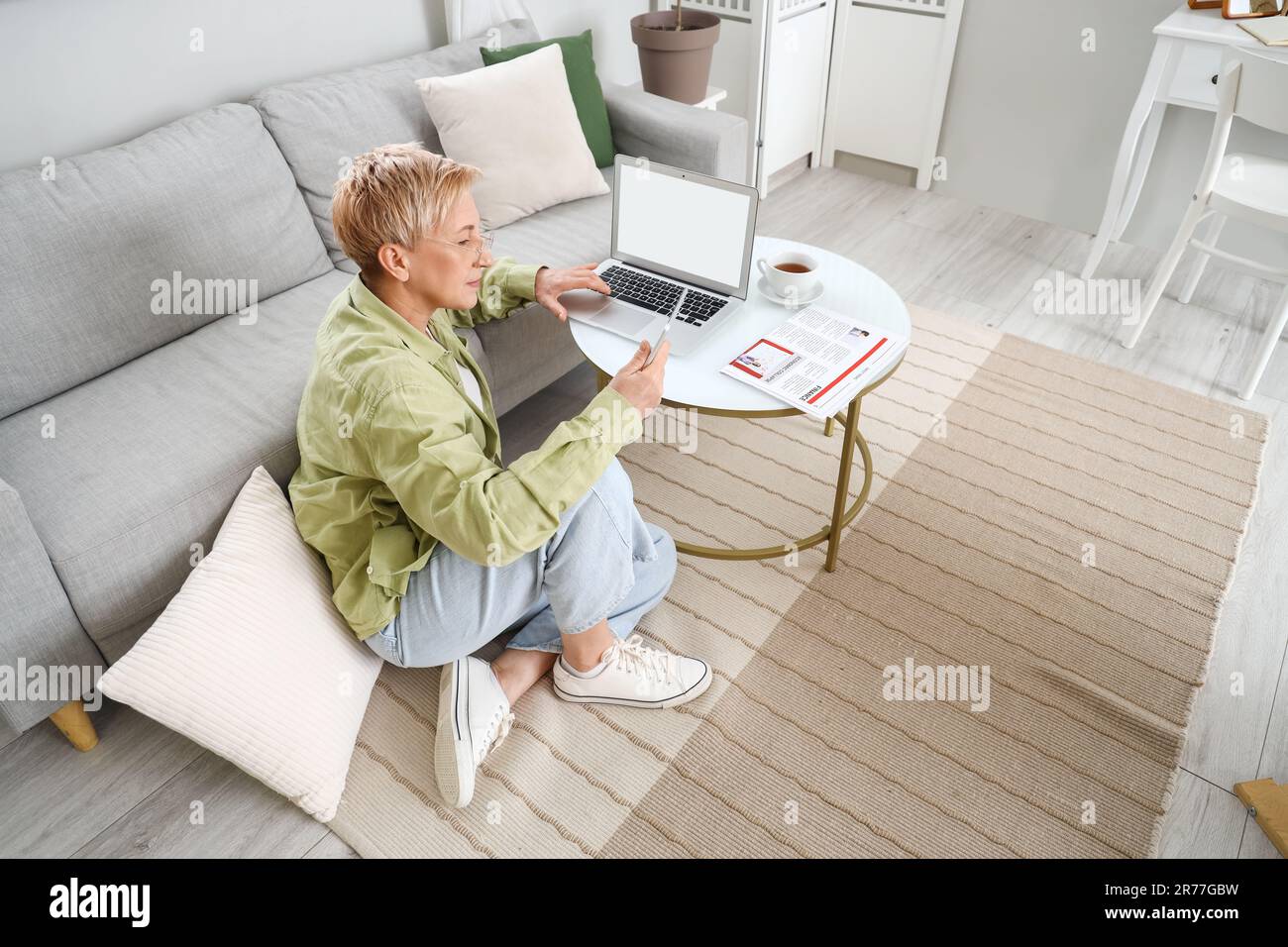 Mature female programmer working with tablet computer and laptop at home Stock Photo