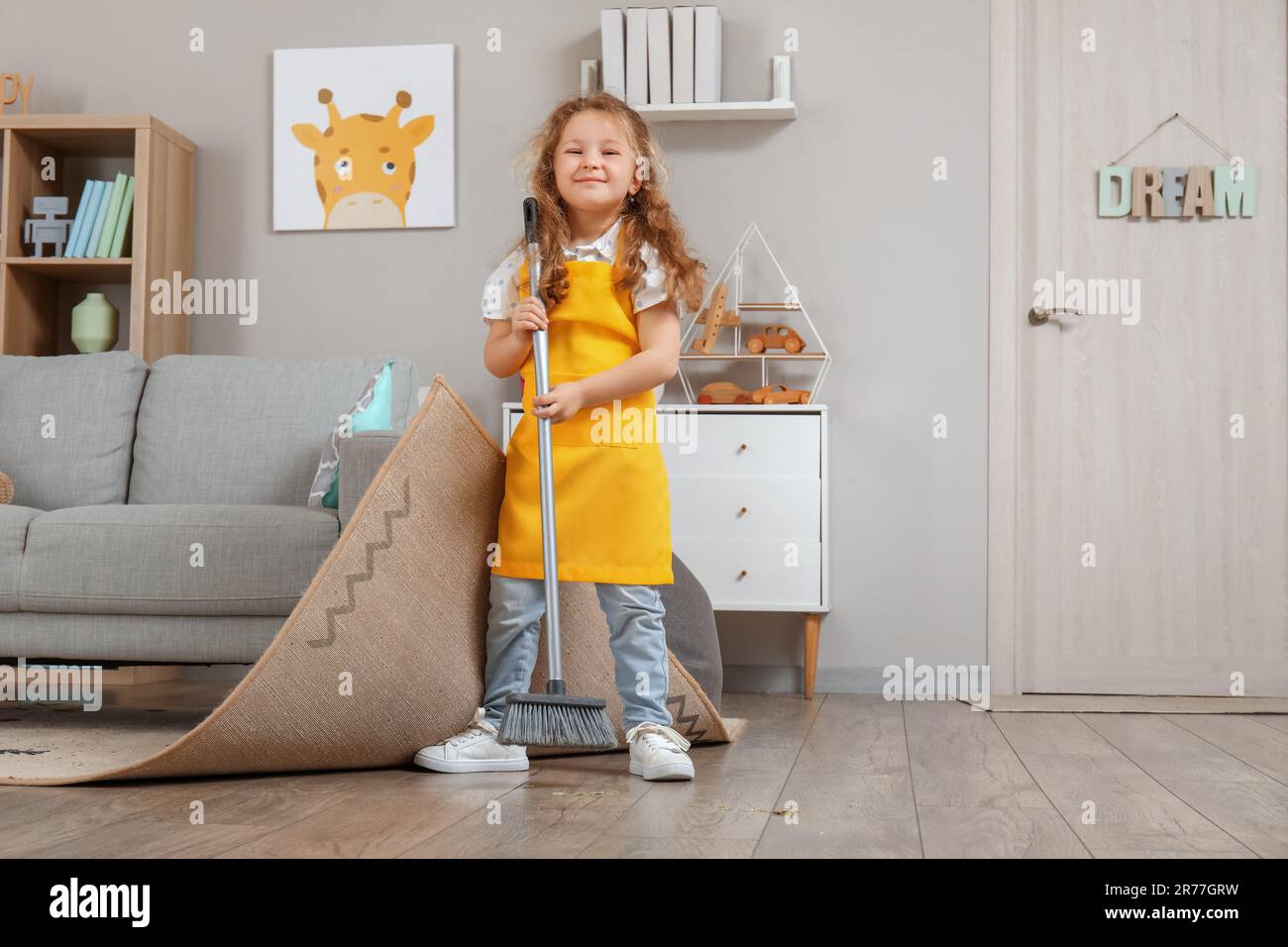 Cute little girl sweeping floor under carpet with broom at home Stock