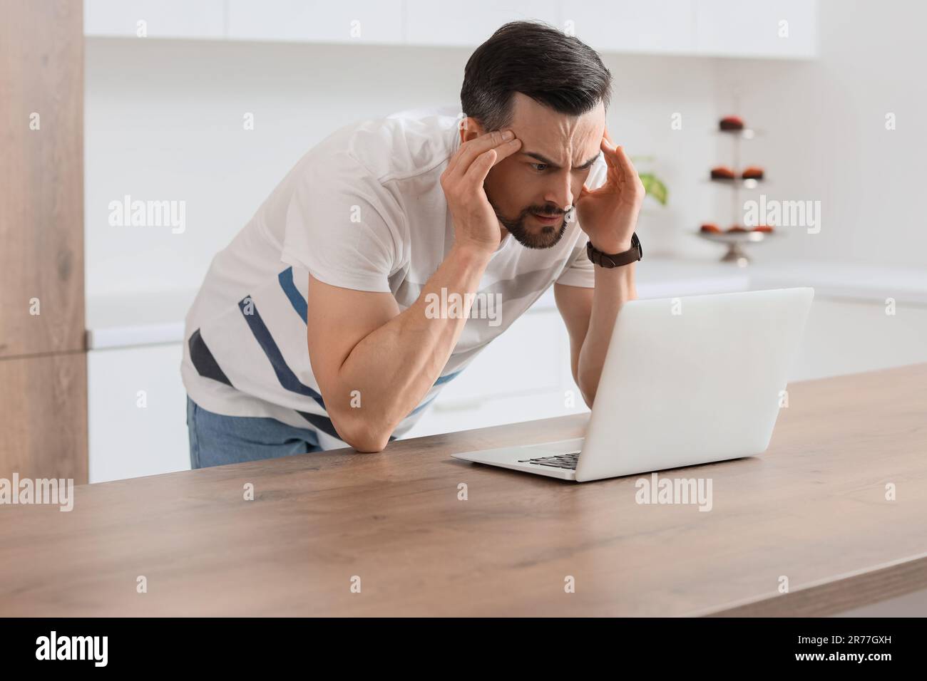 Young man with laptop having panic attack in kitchen Stock Photo