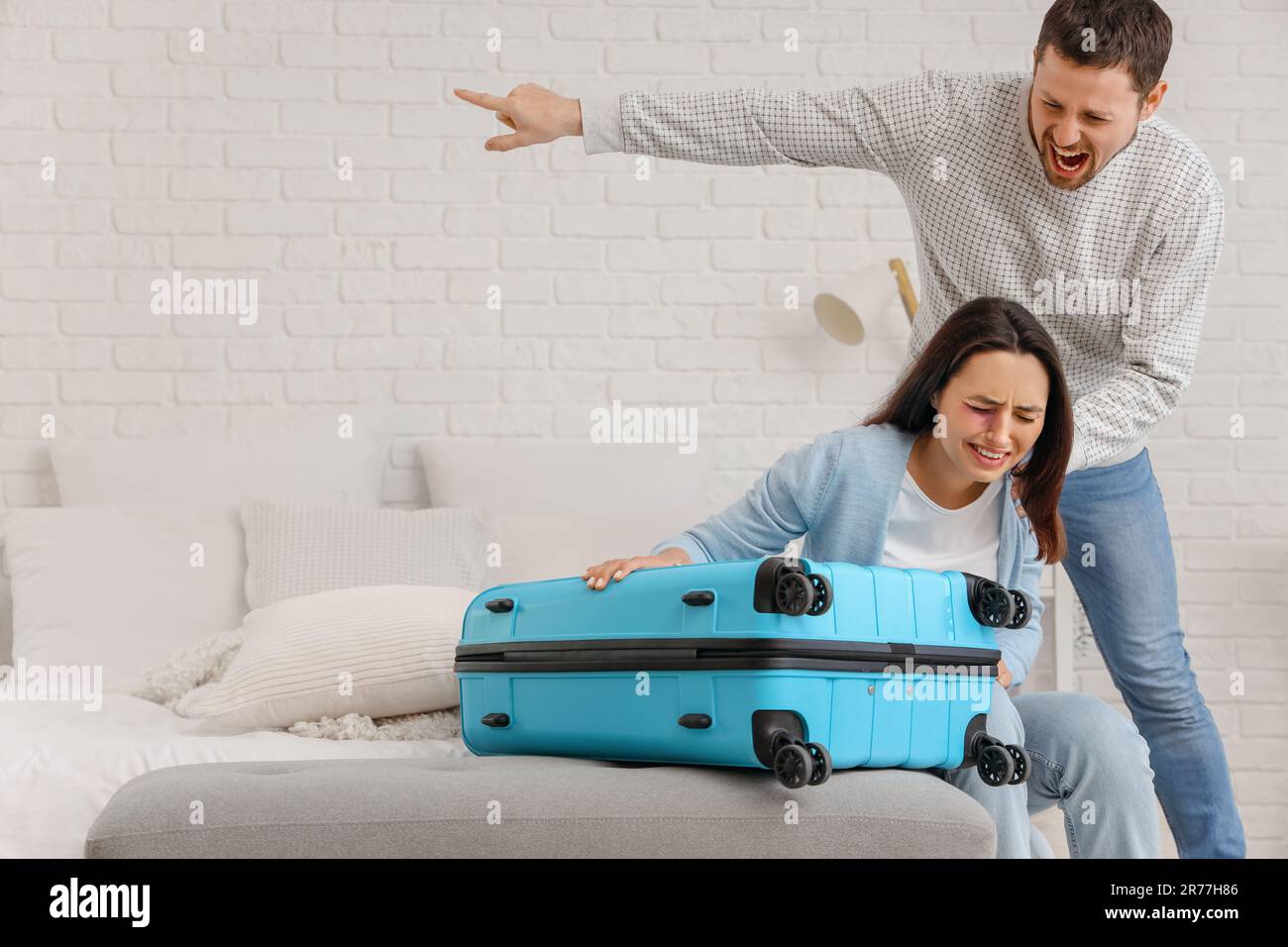 Angry husband kicking his wife with suitcase out in bedroom. Domestic