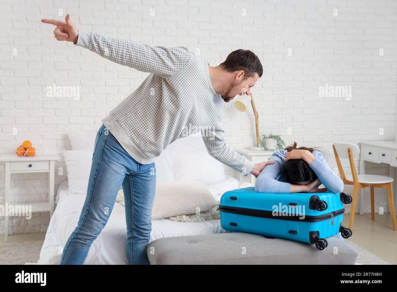 Angry husband kicking his wife with suitcase out in bedroom. Domestic