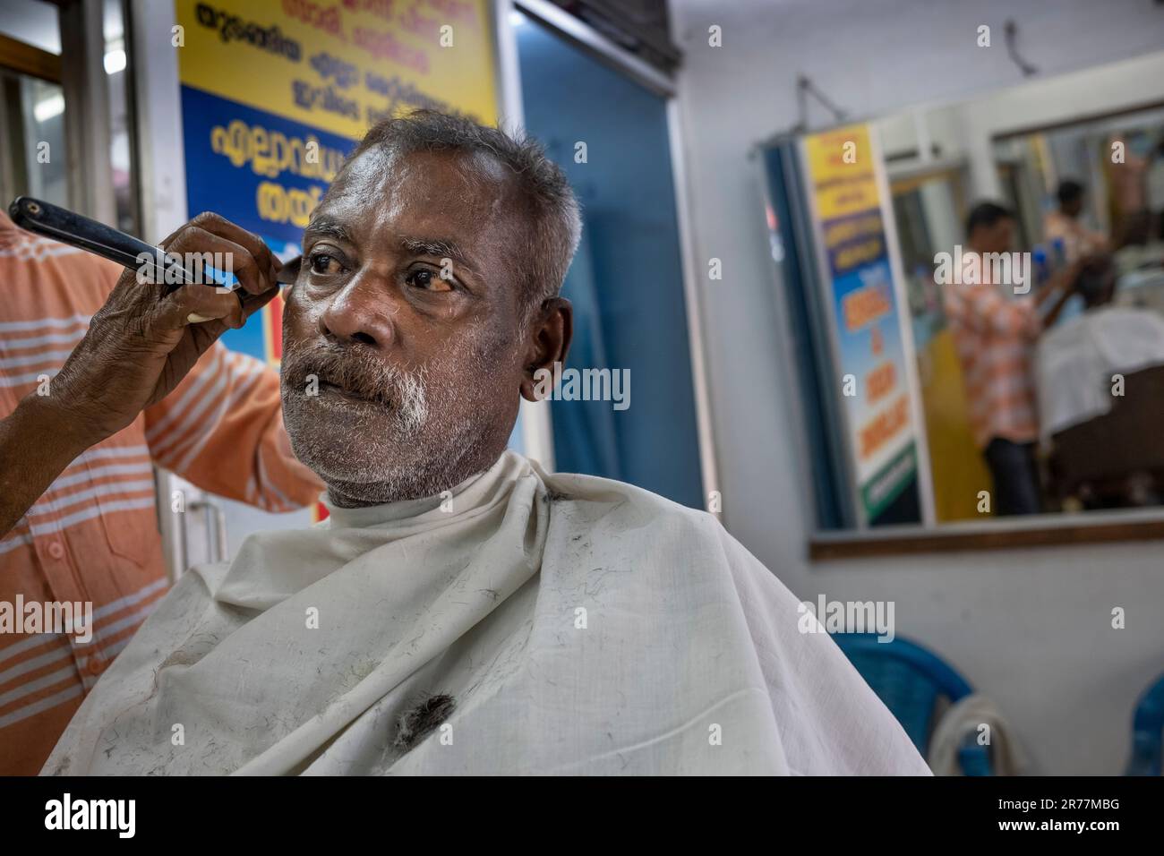 Man receives shave in street side barber shop, colonial Fort Kochi