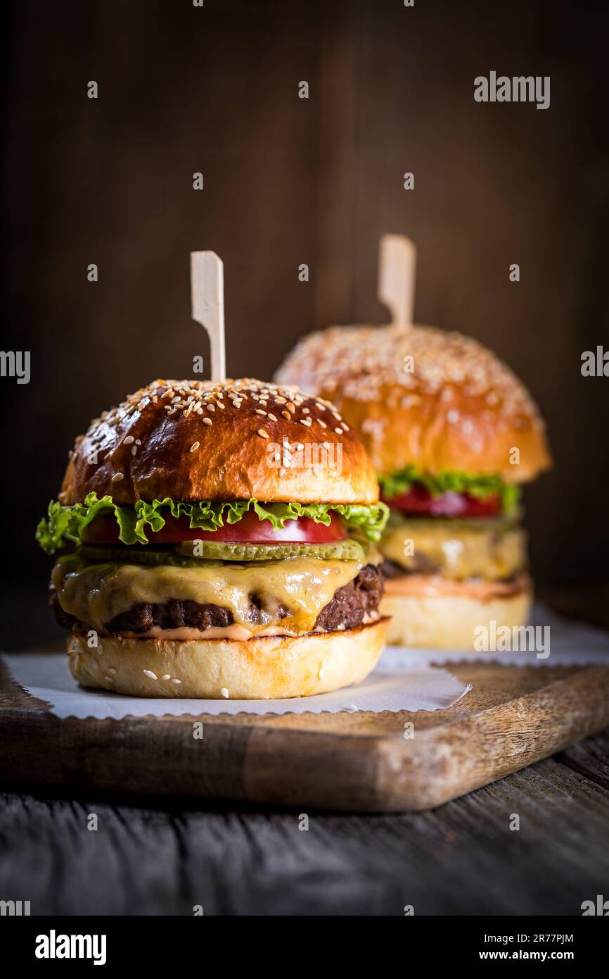 Tasty cheeseburger with lettuce, cheddar cheese, tomato and pickles. Burger bun with sesame seeds. Rustic atmosphere. Delicious fast food meal Stock Photo