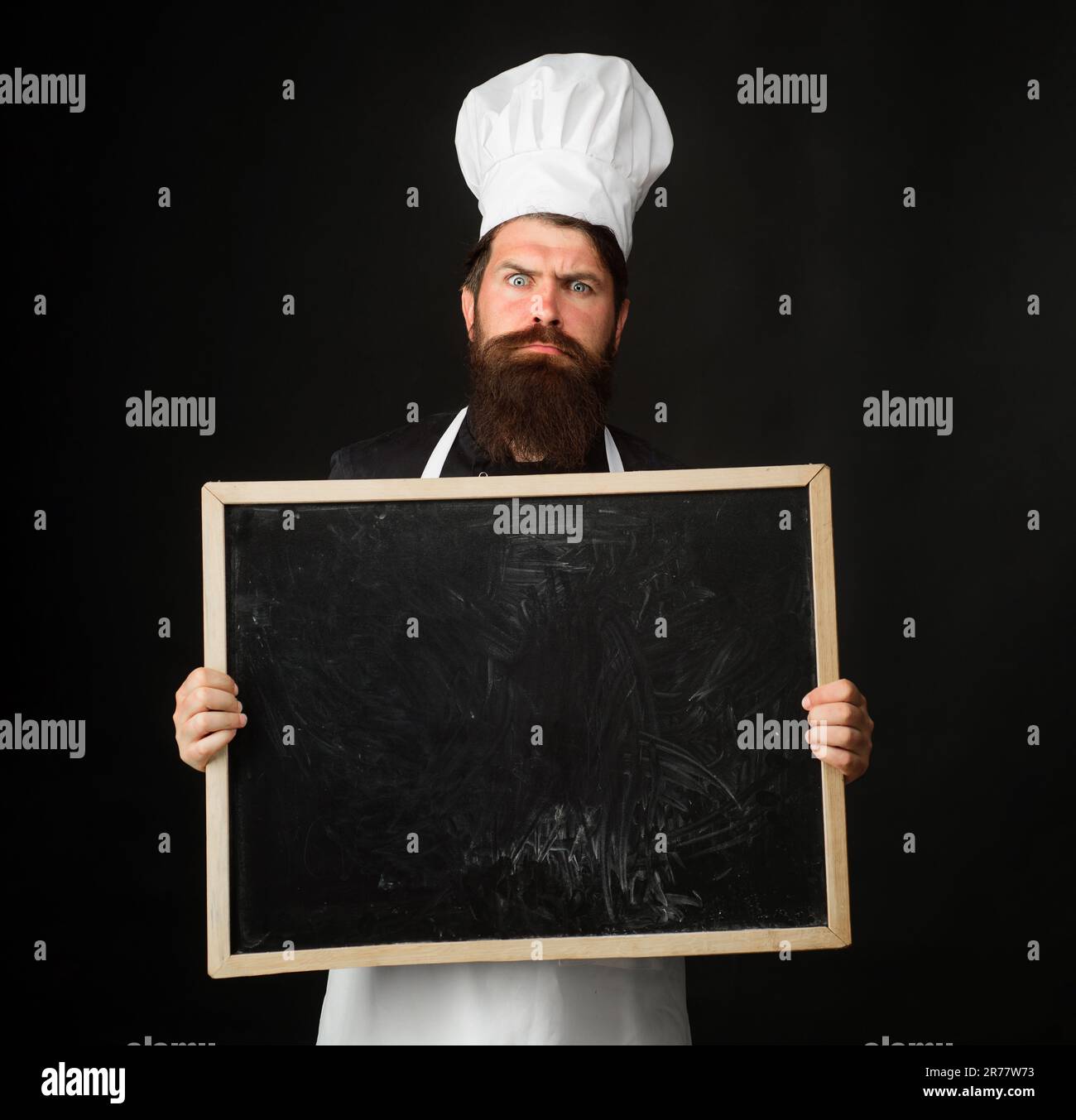 Surprised male chef with blank blackboard. Food preparation. Healthy menu. Cook in uniform and chef hat with empty billboard. Copy space for advertise Stock Photo