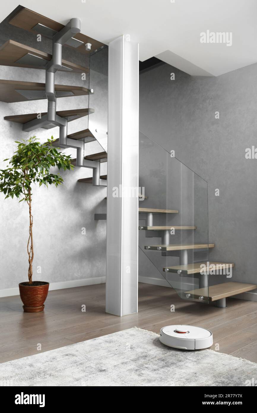 A staircase with wooden steps and an elegant glass fence, a column of matte glass, large indoor flower in the modern interior of the apartment. Stock Photo