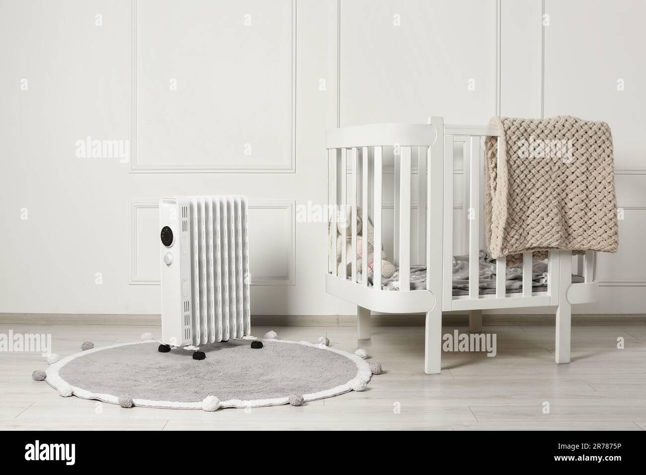 Modern portable electric heater on rug and baby crib indoors Stock Photo