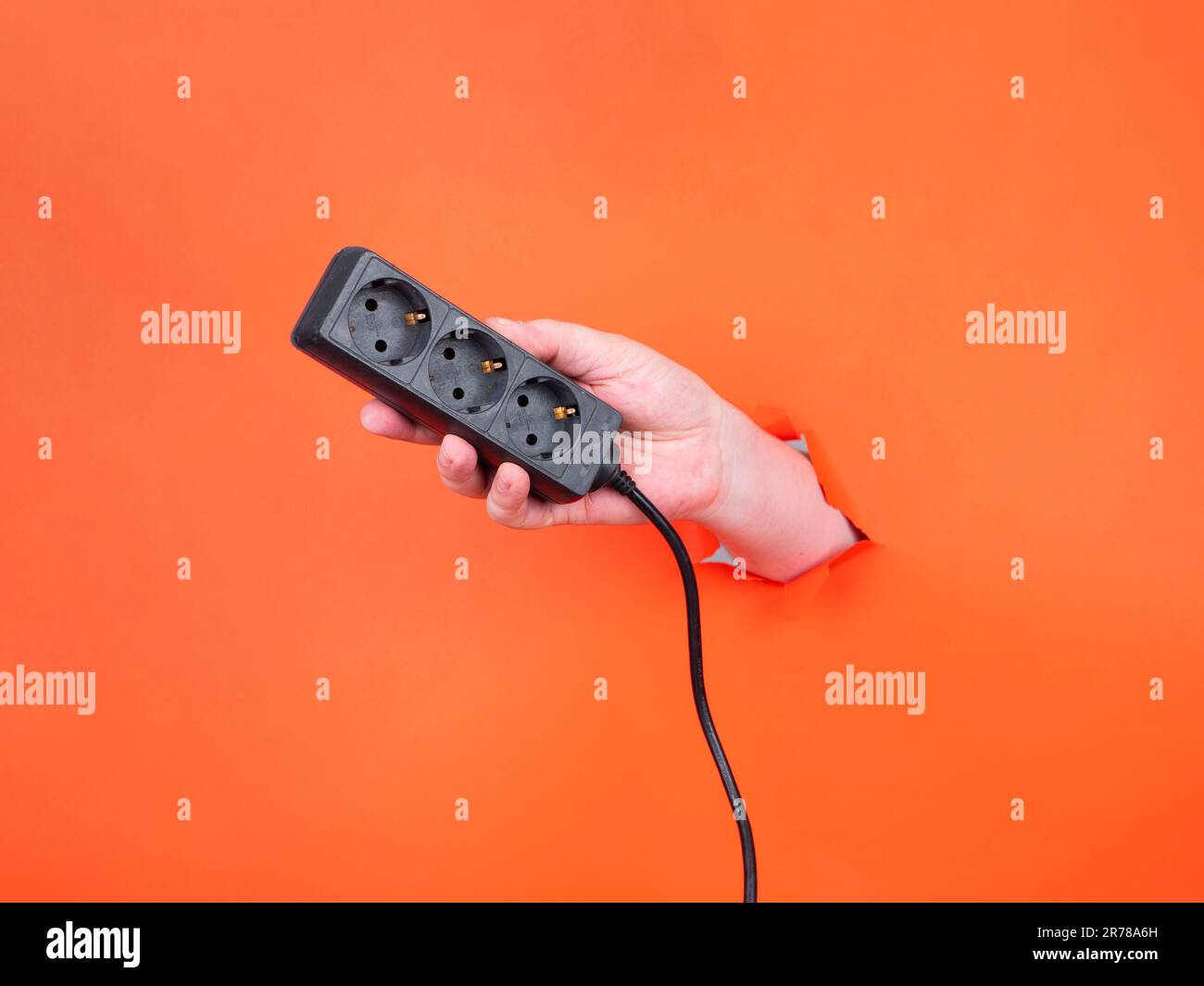 A hand holds a power strip through torn orange paper. No face, copy