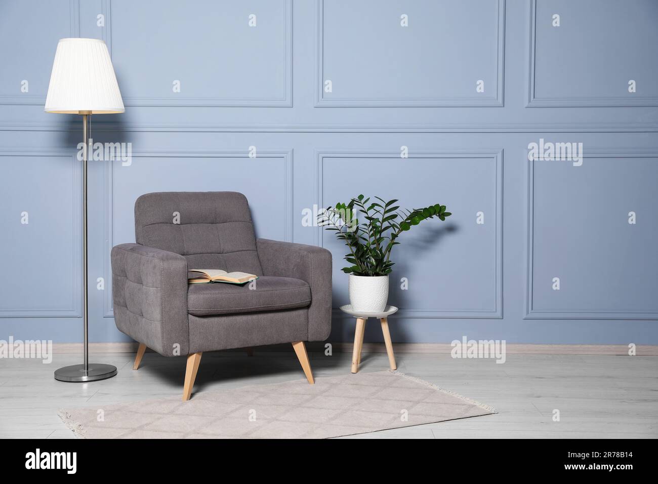 Cosy armchair, floor lamp and potted plant near light grey wall in room ...