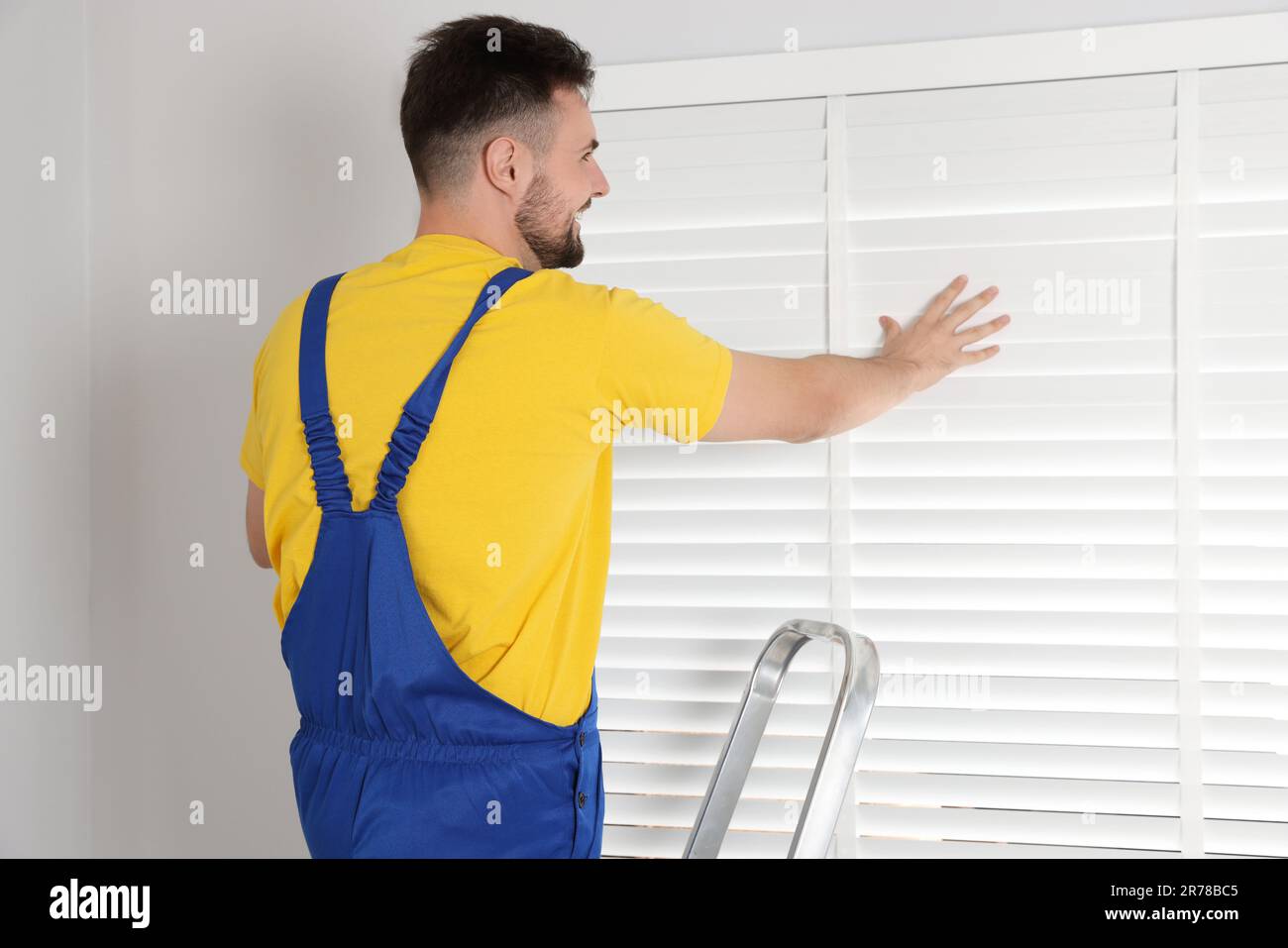 Worker in uniform installing horizontal window blinds indoors Stock Photo